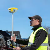 image of a geomax zenith 16, being held by a person working on site, tablet in one hand gnss receiver with the pole on the other.